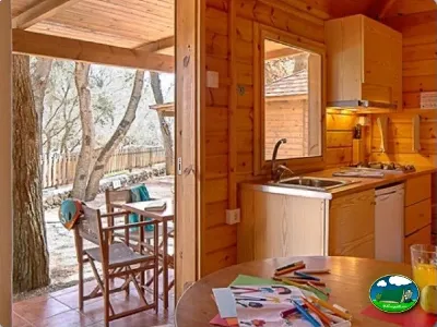 Cabaña de madera con cocina y terraza entre árboles del Camping Son Bou, Alaior (Menorca)