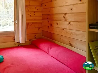 Cabaña interior con cama roja y paredes de madera del Camping Son Bou, Alaior (Menorca)