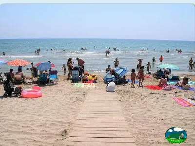 Playa junto al mar con pasarela de madera y bañistas del Camping Bravoplaya, Ribera de cabanes (Castellón)