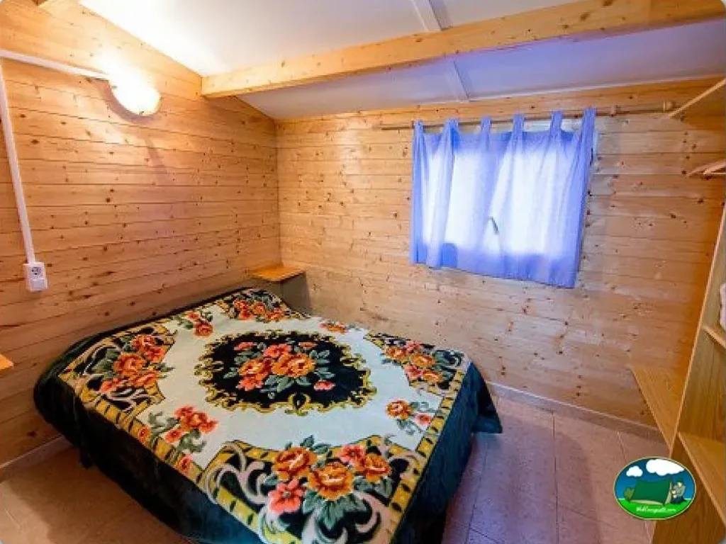 Cabaña de madera interior con cama y ventana del Camping La Tancada, La Ràpita (Tarragona)