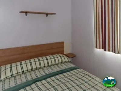 Habitación con cama de madera y cortinas del Camping La Torre del Sol, Montroig (Tarragona)
